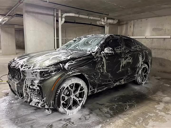Black BMW X6 covered in foam inside a concrete parking garage