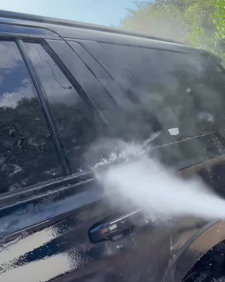 Pressure washer rinsing the side windows of a black Escalade