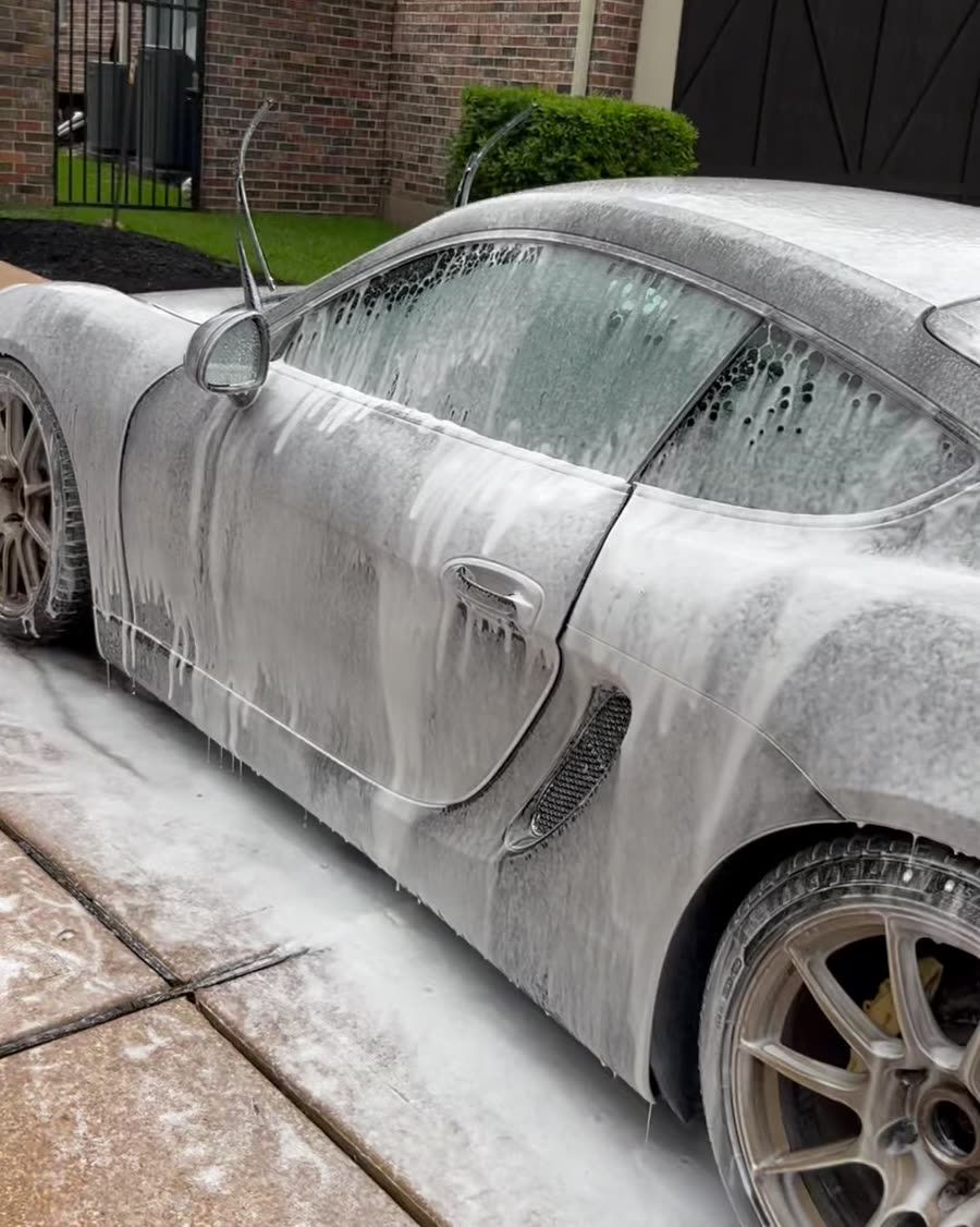 Porsche Cayman covered in thick snow foam during a hand wash in a Houston driveway