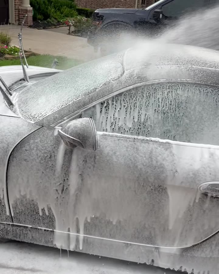 Foam cannon spraying thick suds over a Porsche